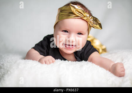 Bella bambina in una T-shirt nera. piccolo sei mesi in studio sul letto Foto Stock