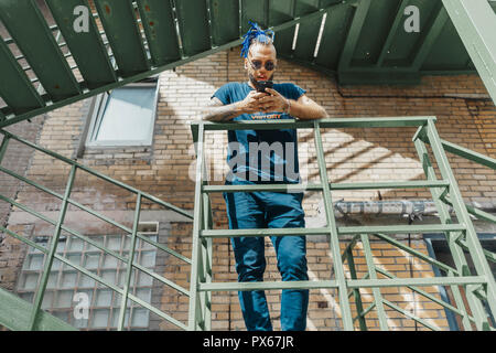 Giovane uomo attraente con blue dreadlocks in piedi alla scala. Foto Stock