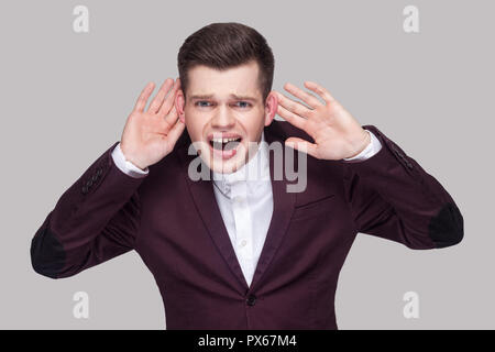 Non riesco a sentire voi. Ritratto di bel giovane in tuta viola e una camicia bianca, in piedi e tenendo le mani sul orecchio e cercando di sentire che cosa ha detto. ind Foto Stock