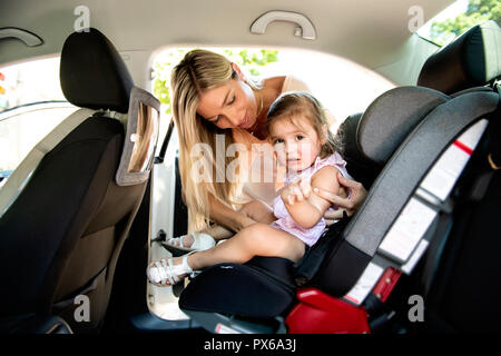 Una madre mettendo la sua figlia del bambino nel suo sedile auto in auto Foto Stock