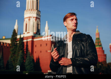 Brutale Man In Black Leather Jacket guarda al lato contro lo sfondo della torre del Cremlino Foto Stock