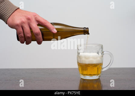 Riempimento di un bicchiere di birra con pinta inzecata dalla bottiglia, versando a mano Ale in un tankard Foto Stock