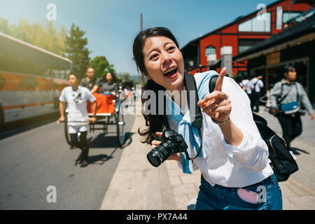 Ragazza gioiosa traveler curiosamente rivolto al cielo con un rickshaw in background. donna uomo lente avente il divertimento in viaggio in Giappone. viaggiare in Kyoto vite Foto Stock