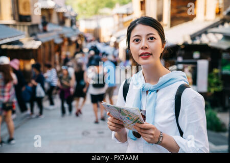 Femmina azienda turistica la mappa e permanente sulla vivace strada in Giappone. traveler ricerca direzione sulla guida della carta in giappone vacanze. straniero indietro Foto Stock