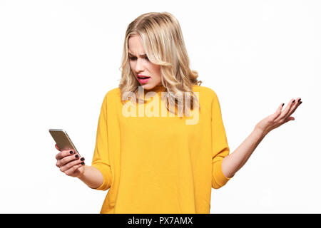 Scioccato arrabbiato giovane donna guardando il suo telefono cellulare per l'incredulità. Donna fissando sconvolgente messaggio di testo sul suo telefono, isolato su bianco backgroun Foto Stock