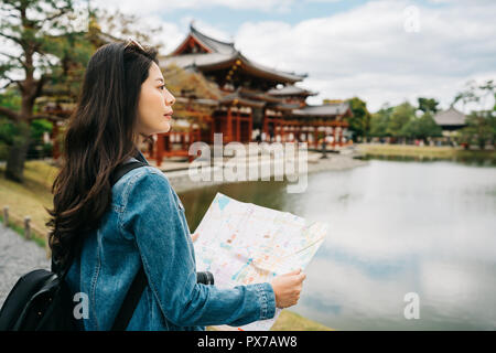 Bella asiatica traveler in piedi vicino al laghetto, tenendo la mappa e guardando la vista. Giappone viaggi vacanze estate ragazza godendo sightseeing in Kyo Foto Stock