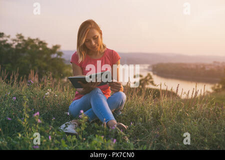 Bella donna gode di libro di lettura con un paesaggio urbano e vista sul fiume dietro di lei. Foto Stock