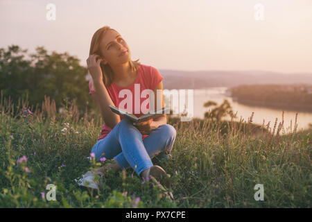 Bella donna gode di libro di lettura con un paesaggio urbano e vista sul fiume dietro di lei. Foto Stock