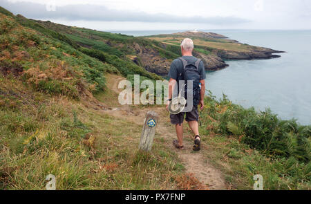 Lone uomo a camminare accanto a un marcatore di legno Post di Point Lynas faro sull'Isola di Anglesey sentiero costiero, Wales, Regno Unito. Foto Stock