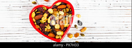 Energy Blend Trail Miti con noci e frutta secca in ciotola a forma di cuore su sfondo di legno Foto Stock