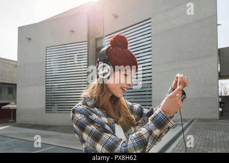 Un giovane hipster donna con i capelli rossi, utilizza un'applicazione nel suo smart phone dispositivo per inviare un messaggio di testo e ascoltare musica Foto Stock