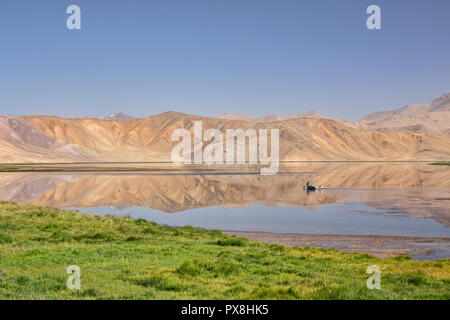 Pescatore solitario righe barca attraverso riflessioni sul lago Bulunkul in Alta Valle Gunt, Bulunkul, Pamir Mountains, il Pamir Highway, Tagikistan Foto Stock