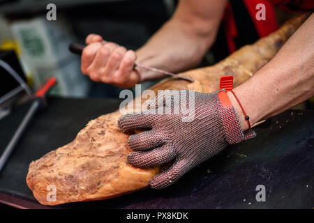 Close-up di macellaio disossare un prosciutto in una moderna macelleria con sicurezza di metallo guanto di maglia Foto Stock