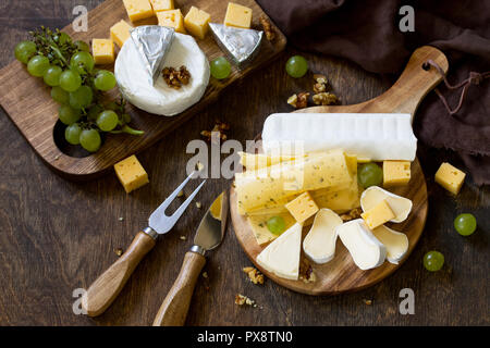 Il piatto di formaggi. Assortimento di formaggi, uva e i dadi sul buio tavola in legno rustico. Foto Stock