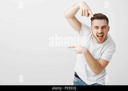 Ci si va. Ritratto di elegante fiduciosi ed emotiva uomo macho con setole e taglio di capelli alla moda puntando alla fotocamera e a sinistra a dare indicazioni per spostare in tal modo con audace espressione fredda Foto Stock