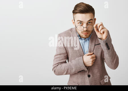 Studio shot di divertenti da stupidi maschio lavoratore di ufficio in camicia alla moda alla moda e acconciatura guardando da sotto gli occhiali toccando rim di occhiali essendo incuriosito ed interessato ascoltando il segreto di un amico Foto Stock