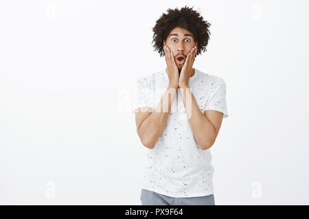 L uomo ha scosso amico è stato licenziato. Scioccato e sorpreso bello ispanico maschio adulto con modello di acconciatura afro, la caduta della mascella, in piedi con la bocca aperta e tenendo le mani sulle guance in posa stupito Foto Stock