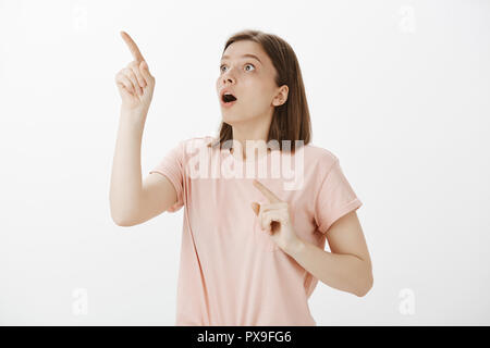 Wow, guarda questa cosa incredibile. Ritratto di impressionato e sorpreso bella donna apnea da stupore, soffocare, di puntamento e di ricerca nell'angolo superiore sinistro, vedendo shooting star Foto Stock