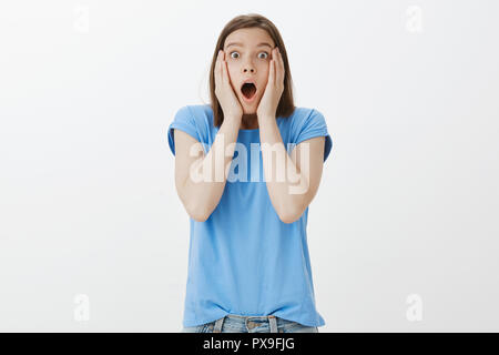 Alcun modo che non può accadere per un reale. Ritratto di impressionato e sconvolto divertente donna in blu t-shirt, la caduta della mascella, gridando e fissando con occhi schioccato in telecamera, tenendo le mani sul viso, storditi Foto Stock