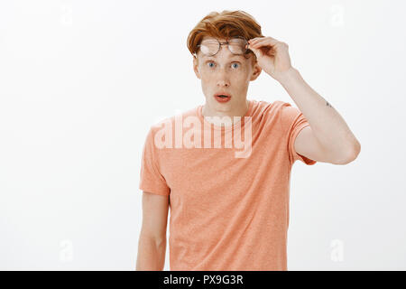 Ritratto di affascinante da stupidi redhead ragazzo con lentiggini in t-shirt e si toglie gli occhiali e guardando con stupore e sorpresa alla fotocamera, essere colpito vedendo incredibilmente affascinante compagno di classe Foto Stock