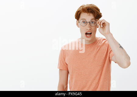 Carino redhead geek maschio discutendo con i nuovi compagni di gioco per computer, parlando con passione ed entusiasmo, toccando rim di bicchieri e fissando entusiasti alla fotocamera, in piedi su sfondo grigio Foto Stock