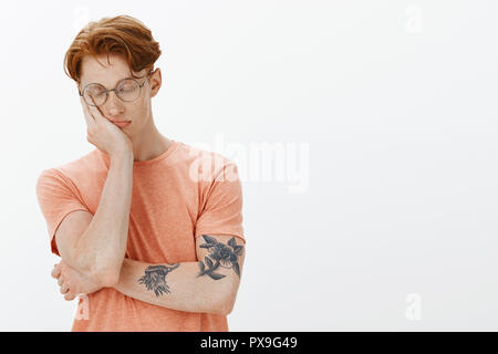 Bella tatuati redhead sensazione di stanchezza, non avendo il sonno prima di esame, poggiando su Palm e il sonno, avente nap mentre in piedi su uno sfondo grigio con gli occhi chiusi e espressione di calma Foto Stock