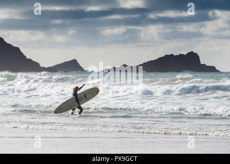 Un surfista portando la sua tavola da surf e in esecuzione nel mare a Fistral Beach in Newquay in Cornovaglia. Foto Stock