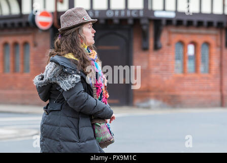 Vista laterale di una donna di mezza età a piedi caldi indossare abiti colorati e un cappotto invernale e hat. Signora indossando vestiti colorati. Foto Stock