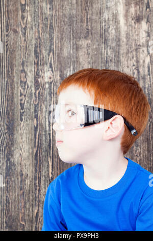 I capelli rossi ragazzo di aspetto europeo durante la riproduzione di builder, vestito sulla testa di occhiali di protezione trasparente Foto Stock