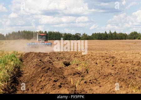 Trattore grande con un aratro di aratri il suolo sul campo dopo il raccolto per la semina di un nuovo raccolto di piante agricole Foto Stock