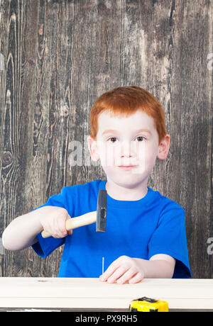 I capelli rossi ragazzo di aspetto europeo per la costruzione di una struttura in legno, nella sua mano impugna un martello e chiodi Foto Stock