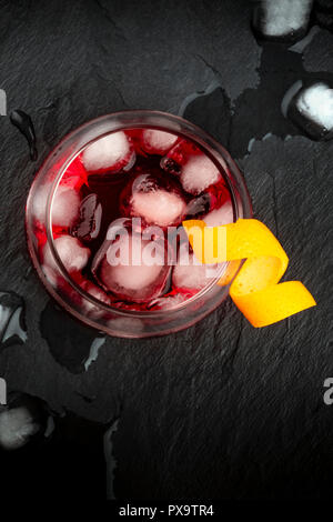 Una foto aerea di un vivace cocktail Negroni con Campari e un tocco di colore arancione guarnire, ripresa dall'alto, con cubetti di ghiaccio su uno sfondo nero, con spazio di copia Foto Stock