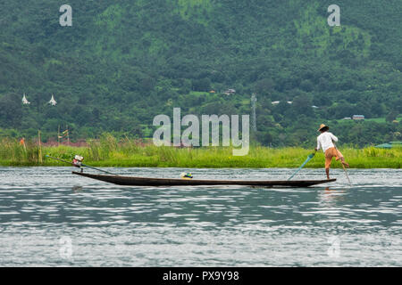 Viaggi, i pescatori locali in una camicia bianca e arancione shorts in equilibrio su un piede sulla punta della barca e tirando net per raccogliere pesci, Lago Inle Birmania Foto Stock