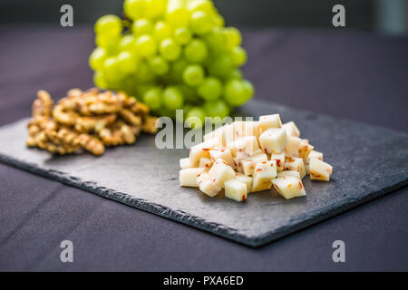 Pezzi di formaggio di uva succosa e noci sulla scheda di ardesia. Foto Stock