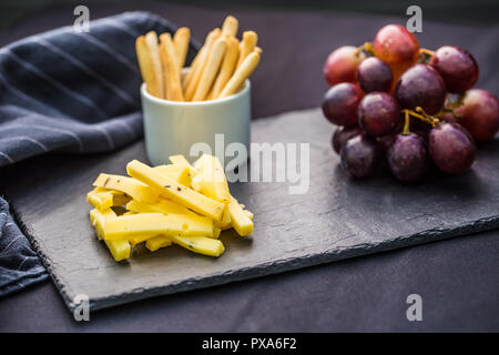Pezzi di formaggio di uva succosa e noci sulla scheda di ardesia. Foto Stock