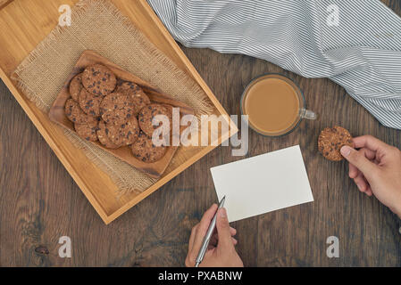 Vista dall'alto - biscotti con scaglie di cioccolato sulla piastra, un bicchiere di latte e la scrittura di messaggio su una tavola di legno Foto Stock