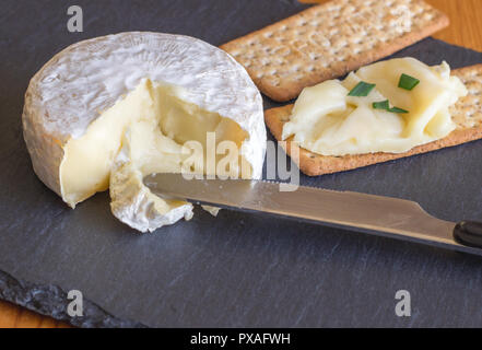 Formaggio Camembert essendo spalmato su cracker sul formaggio scheda di ardesia Foto Stock