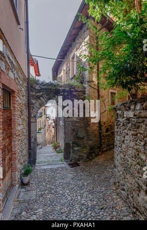 Paesaggio con ripide scale di pietra sotto arco in stretto vicolo al lago turistico villaggio, girato in caduta luminosa luce a San Siro, Como, Italia Foto Stock