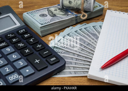 Calcolatrice, dollari, notebook e penna giacciono su di un tavolo di legno. Foto Stock