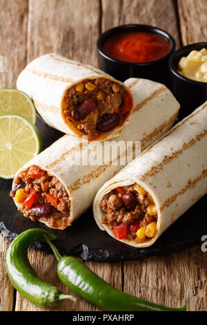 Messicano burrito grigliata con carne di manzo, fagioli, mais, pepe e pomodori servite con salse close-up sul piano verticale. Foto Stock