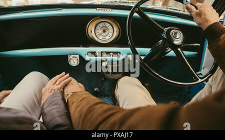 In prossimità di una coppia senior tenendo le mani durante la guida di un'auto. Il vecchio uomo alla guida di auto con donna seduta sul sedile del passeggero tenendo la sua mano. Foto Stock