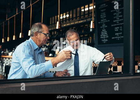 Maturare la gente di affari guardando laptop e discutere di lavorare presso il cafe. Due partner commerciali riuniti in un ristorante. Foto Stock