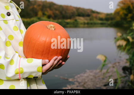 I bambini con le mani in mano in possesso di una zucca arancione sulla sponda del fiume. Halloween. Foto Stock