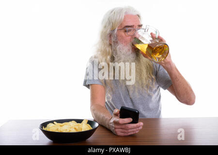 Studio shot di senior uomo barbuto usando il cellulare mentre bere Foto Stock