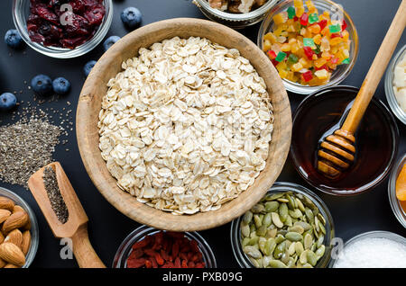 Ingredienti per cereali fatti in casa: avena, chia e semi di zucca, mirtilli e mandorle, noci di cocco e nettare di agave, goji bacche e mirtilli freschi. Foto Stock