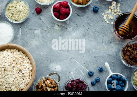 Ingredienti per cereali fatti in casa: avena, di canapa e di semi di zucca, mirtilli e uva passa, noci e mandorle, noci di cocco e miele di mirtilli freschi e Foto Stock