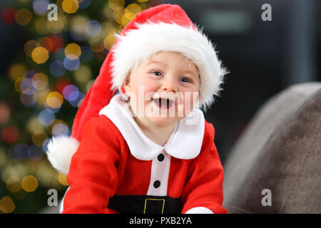 Allegro baby vestiti da Babbo Natale su un lettino a casa a Natale con un albero in background Foto Stock