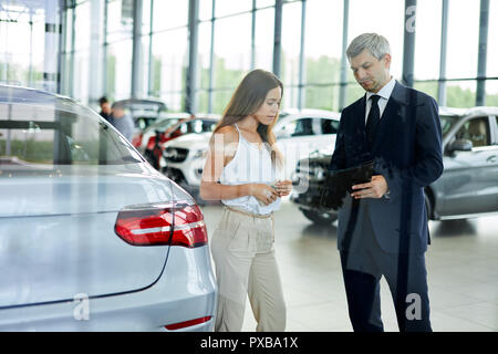 Giovani femmine cliente chiedendo coppia sales manager per aiutare nella concessionaria auto. Foto Stock