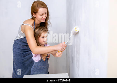 Riparazione nell'appartamento. La famiglia felice la madre e la figlia in grembiuli dipingere la parete con vernice bianca. Madre contribuisce a sua figlia di dipingere la parete con Foto Stock