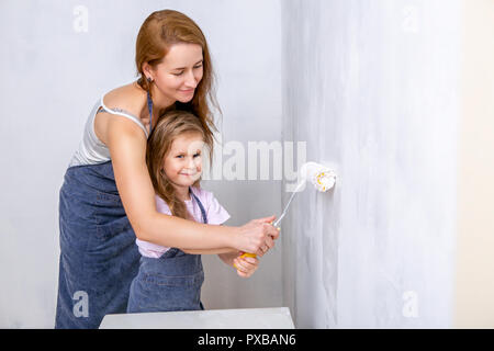 Riparazione nell'appartamento. La famiglia felice la madre e la figlia in grembiuli dipingere la parete con vernice bianca. Madre contribuisce a sua figlia di dipingere la parete con Foto Stock